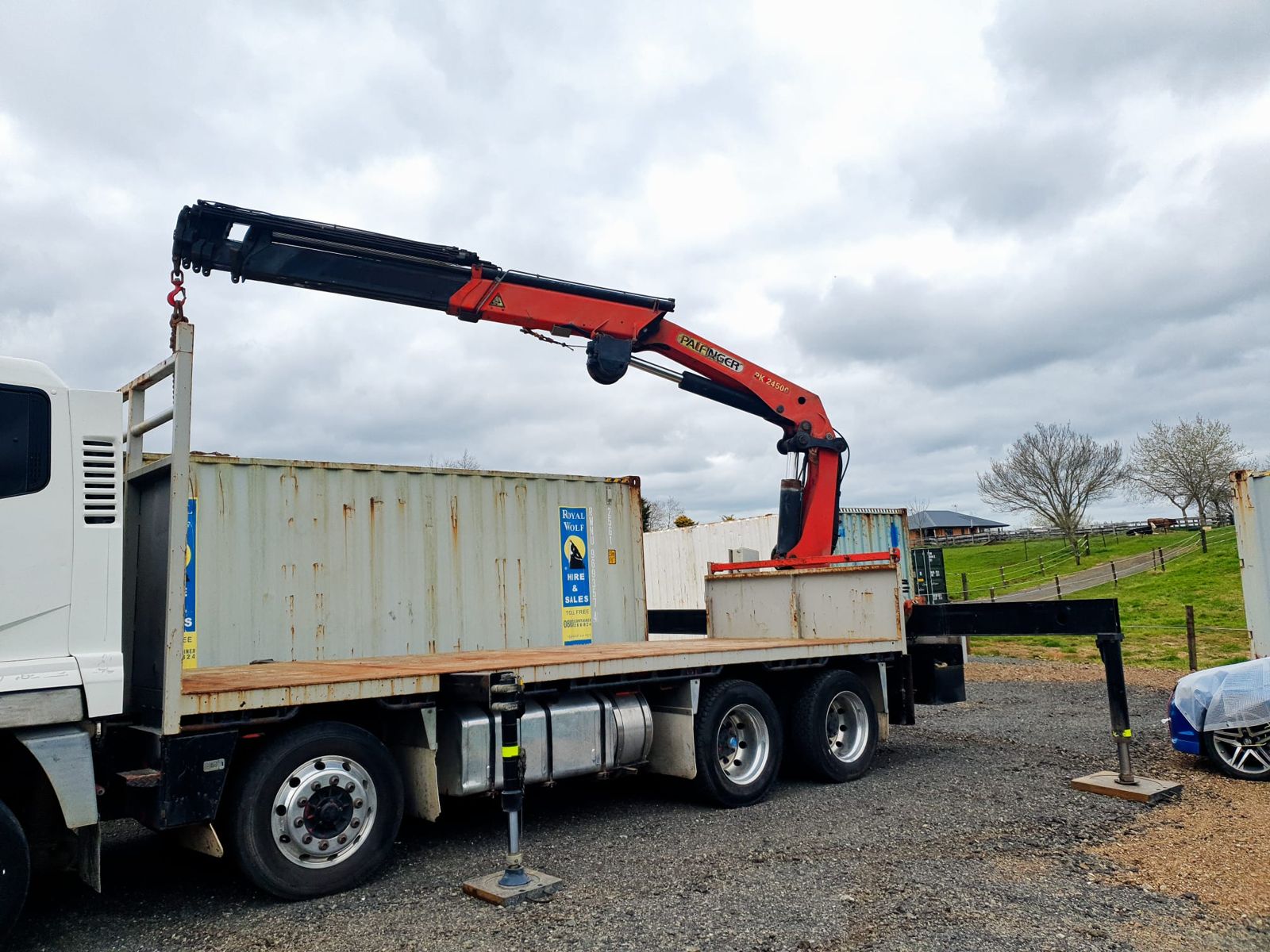 A 20 ft shipping container on the flat deck of the crane truck, crane hooked on, outriggers down