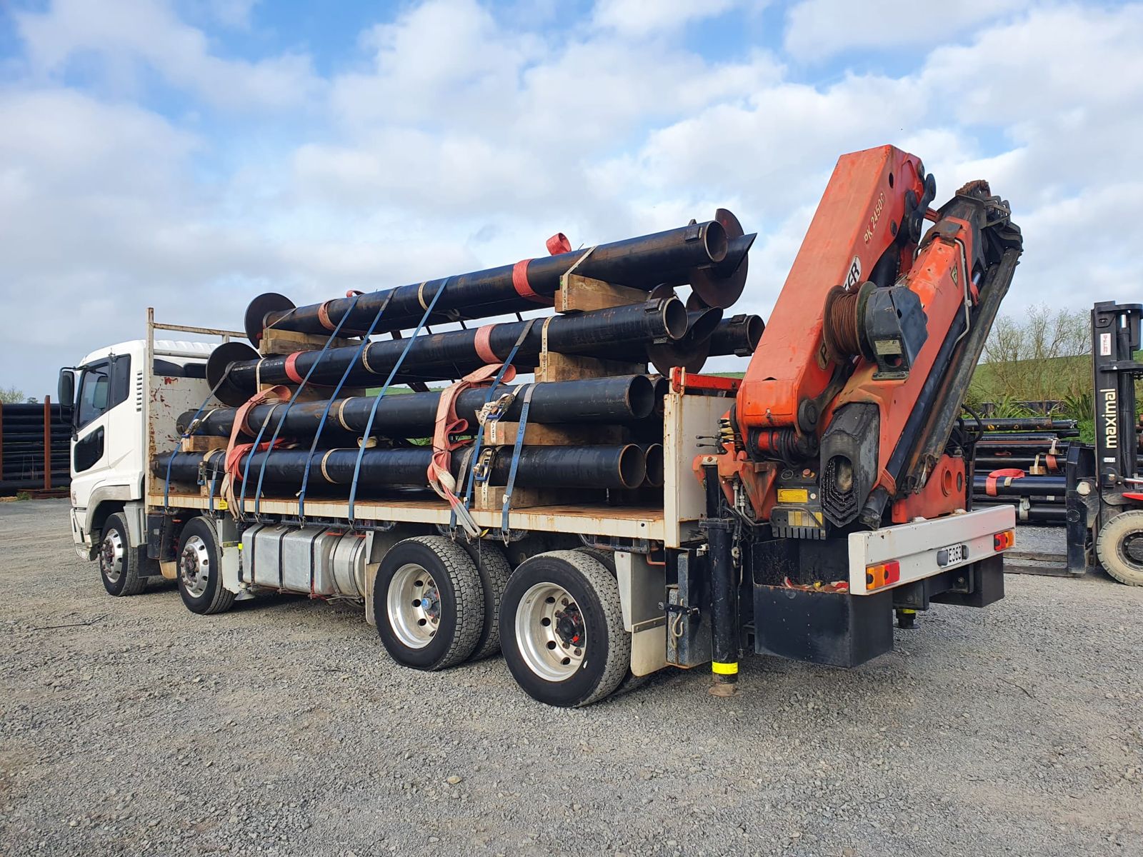 Rear three-quarter view of the loaded truck with steel pipe strapped on the deck, crane folded at the rear