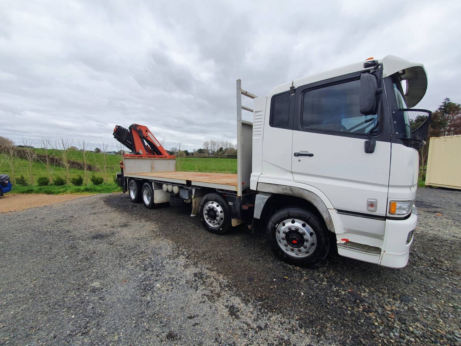The crane truck side-on with its long flat deck empty and the Palfinger crane folded behind the cab