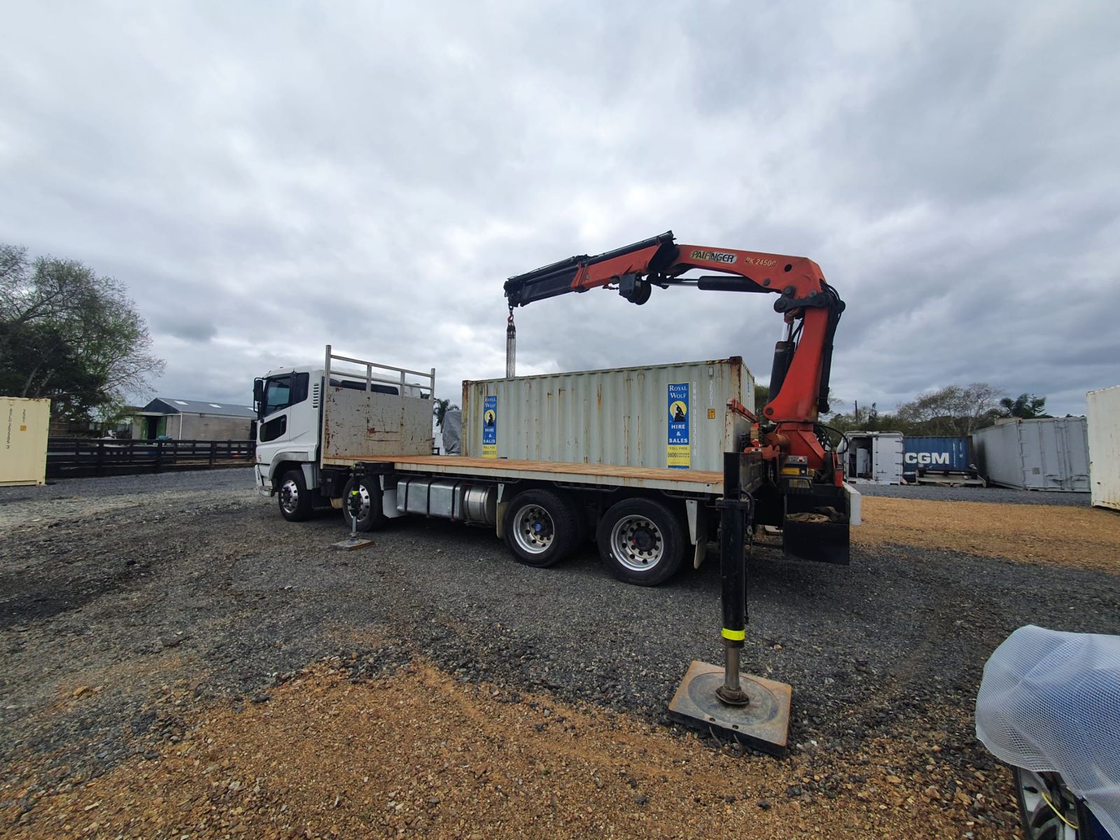 The crane truck on a gravel yard with outrigger down and the crane lifting at a shipping container